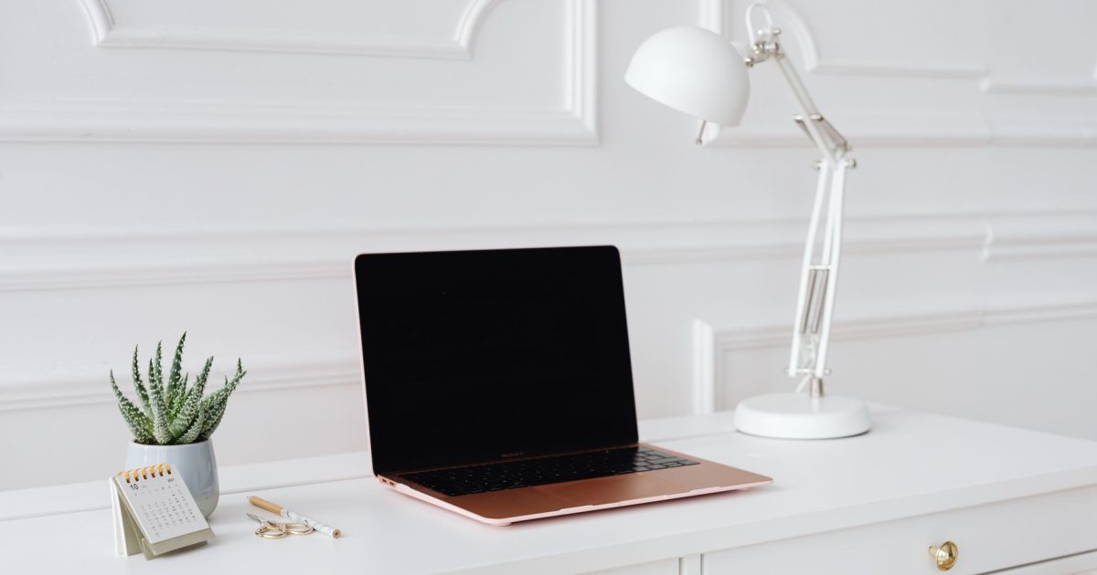 A clean and elegant workspace featuring a laptop, desk lamp, and plant on a white desk.