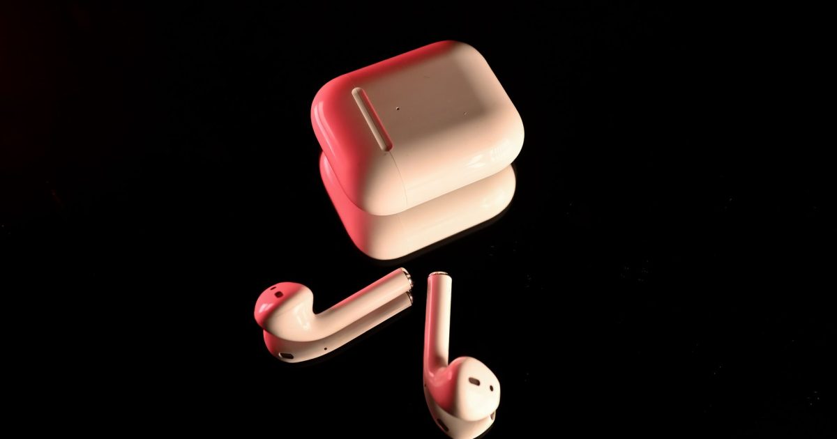 White wireless earbuds with a charging case, highlighted with red lighting on a reflective black surface.