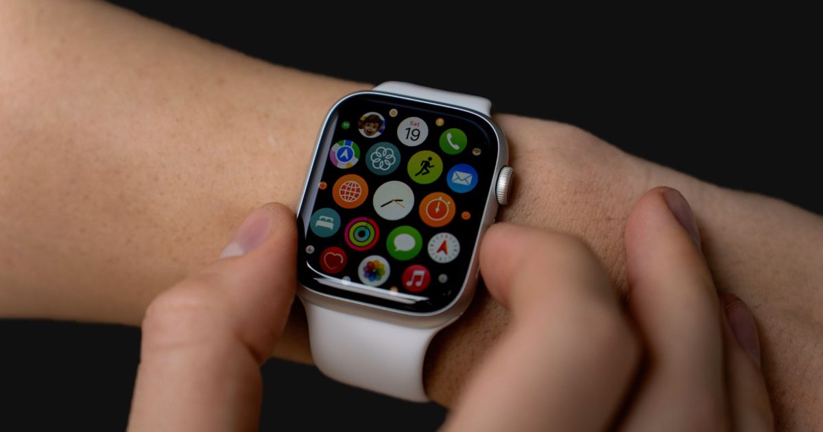 Close-up of person interacting with a smartwatch displaying apps on a dark background.