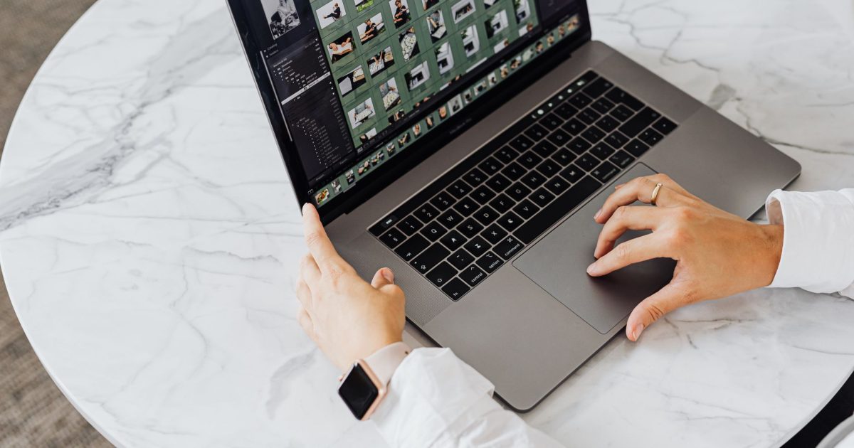 Hands editing photos on laptop, modern workspace on marble table.