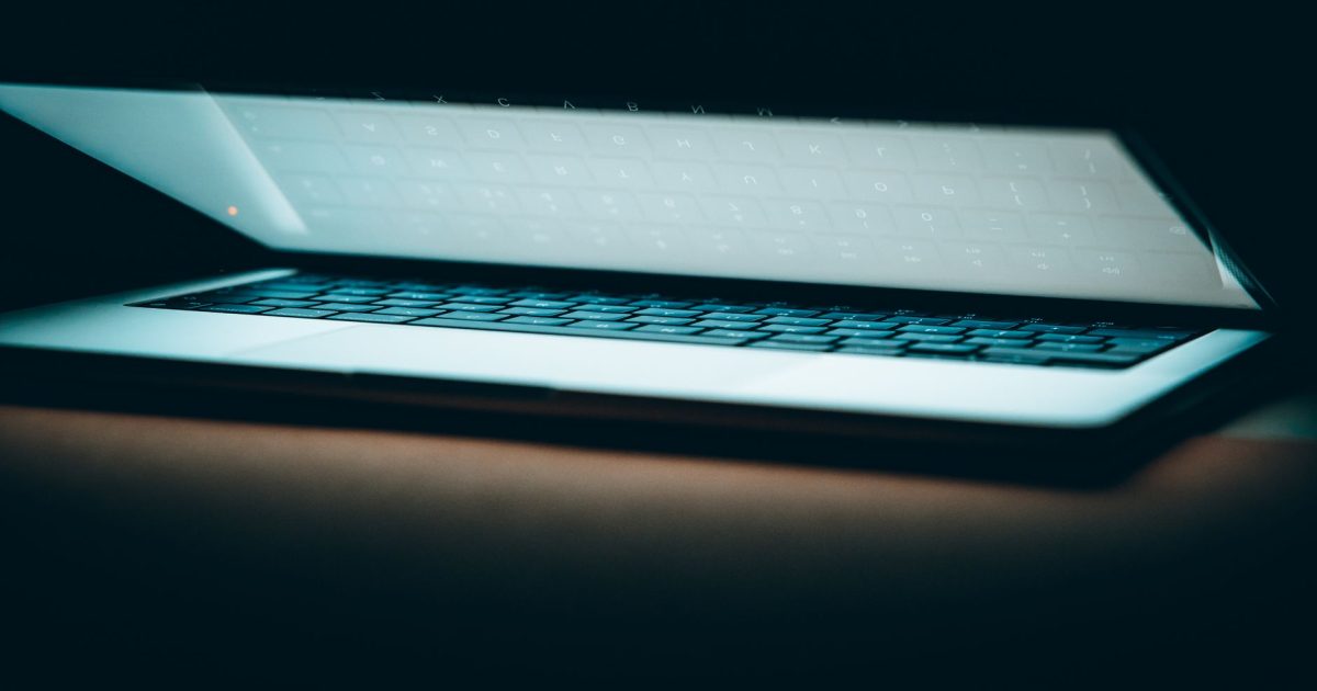 A close-up of a partially open laptop on a wooden surface, displayed in a moody lighting.