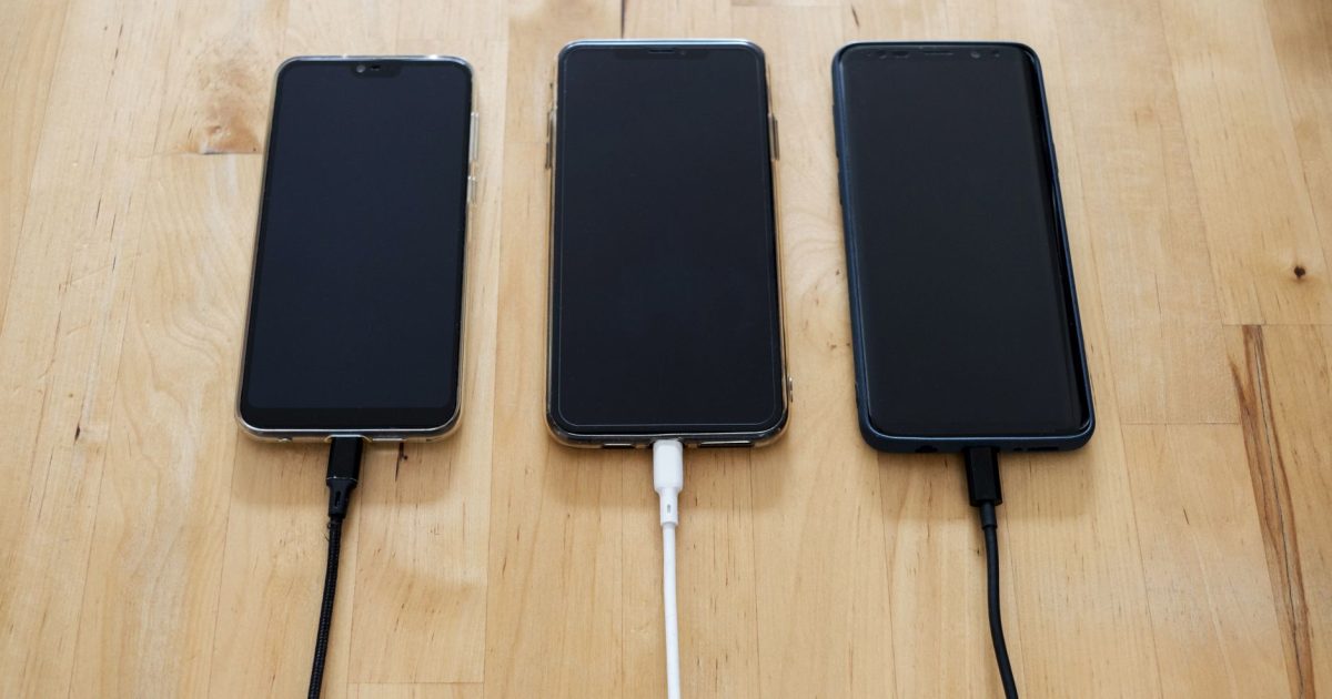 Three smartphones connected to chargers on a wooden surface, showcasing modern technology