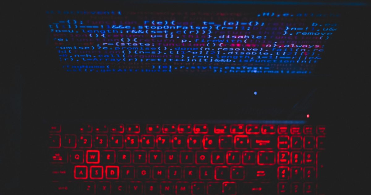 Dark-themed laptop setup with a red glowing keyboard and code on screen, ideal for tech enthusiasts.