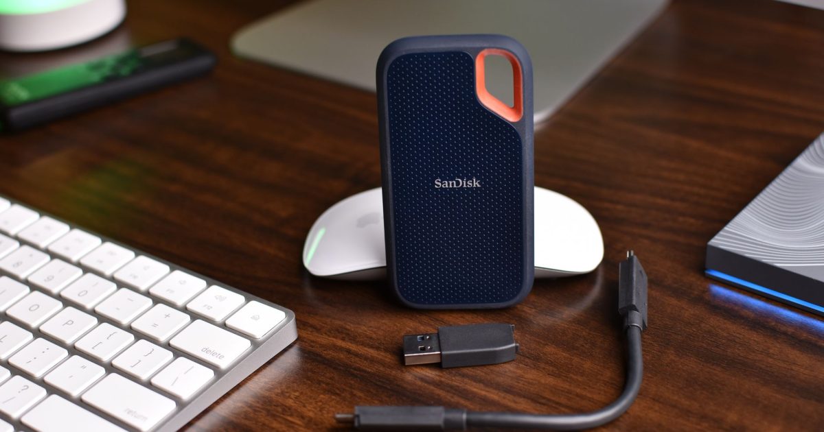 SanDisk portable SSD with USB cable and computer accessories on a wooden desk.