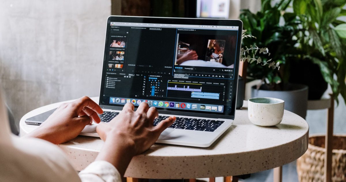 Freelance video editor working on a laptop in a cafe setting, utilizing Adobe software.
