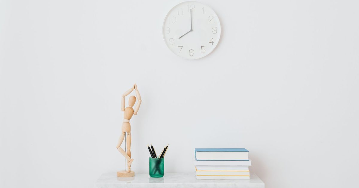 A minimalist workspace setup featuring books, a clock, and decorative elements on a white wall.