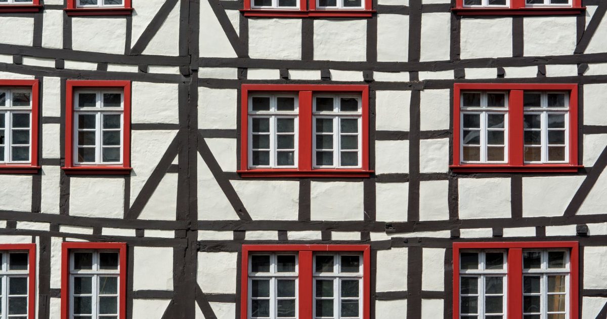 Detailed view of a half-timbered building facade featuring red window frames and geometric patterns.