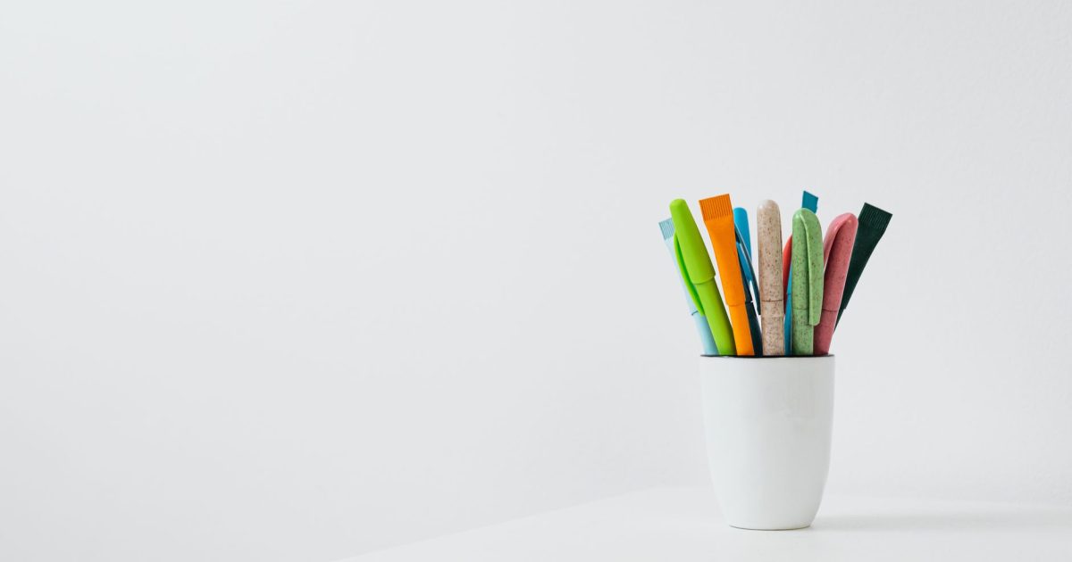Colorful pens in a ceramic cup on a white desk with ample copy space for creative works.