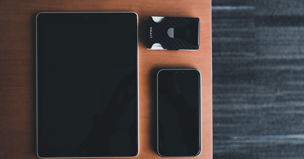 Top view of a tablet, smartphone, and card holder on a wooden surface, showcasing minimalist design.