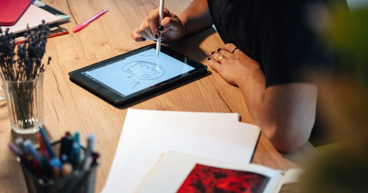 A person drawing on a digital tablet in a creative workspace, surrounded by art supplies.