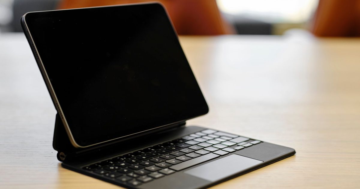 A digital tablet attached to a keyboard case on a wooden table in an office setting.