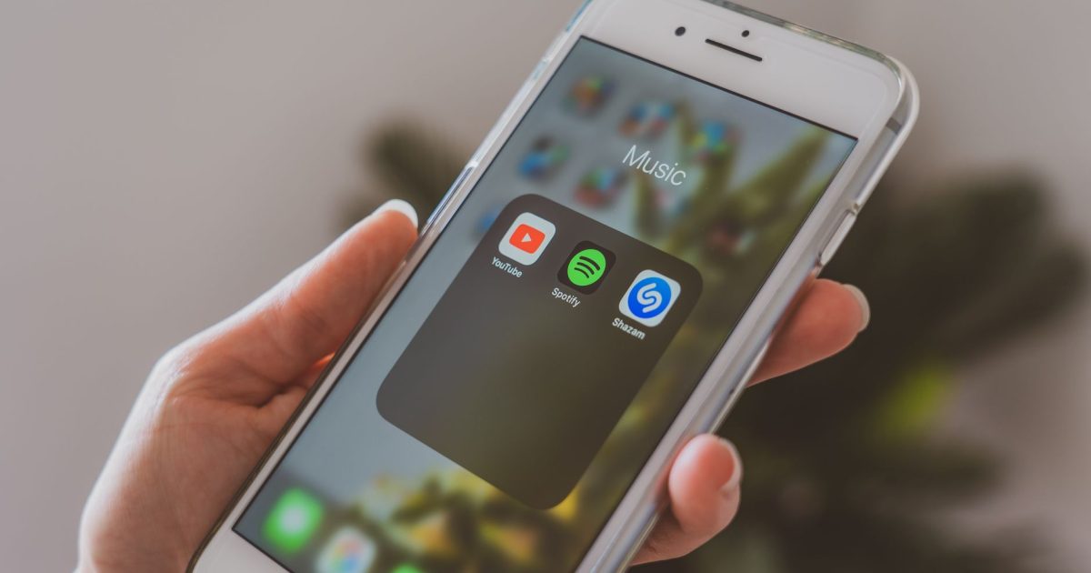 Hand holding a smartphone displaying popular music apps like Spotify and Shazam in a close-up shot.