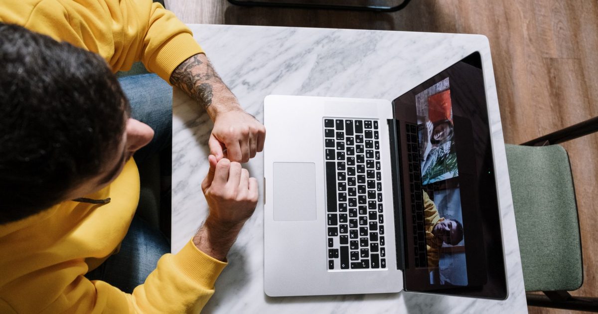 Overhead view of man in yellow sweater video calling on laptop from a marble table.