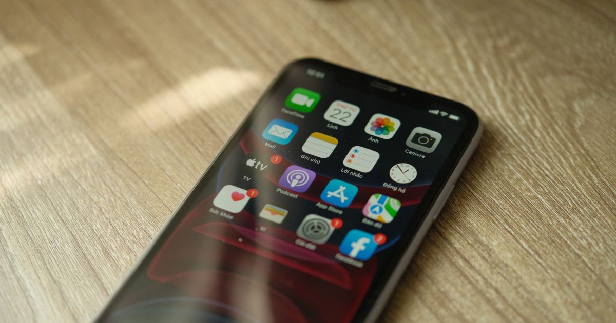 A close-up view of a smartphone displaying various apps on a wooden surface.