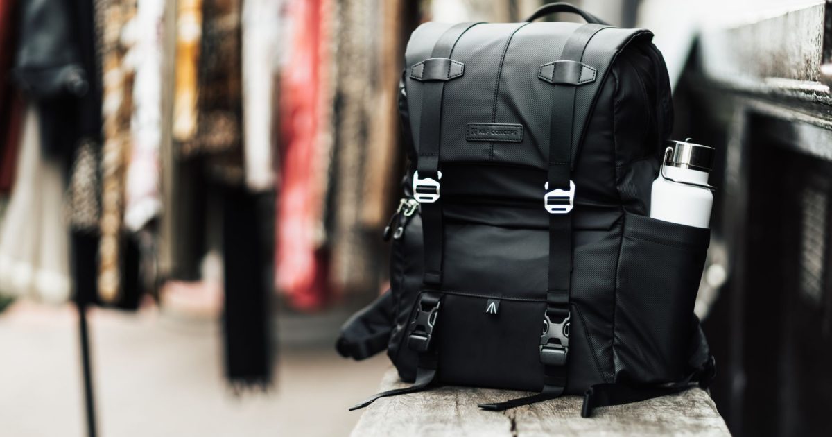 A modern black backpack with a water bottle sits on a wooden bench, ideal for travel enthusiasts.