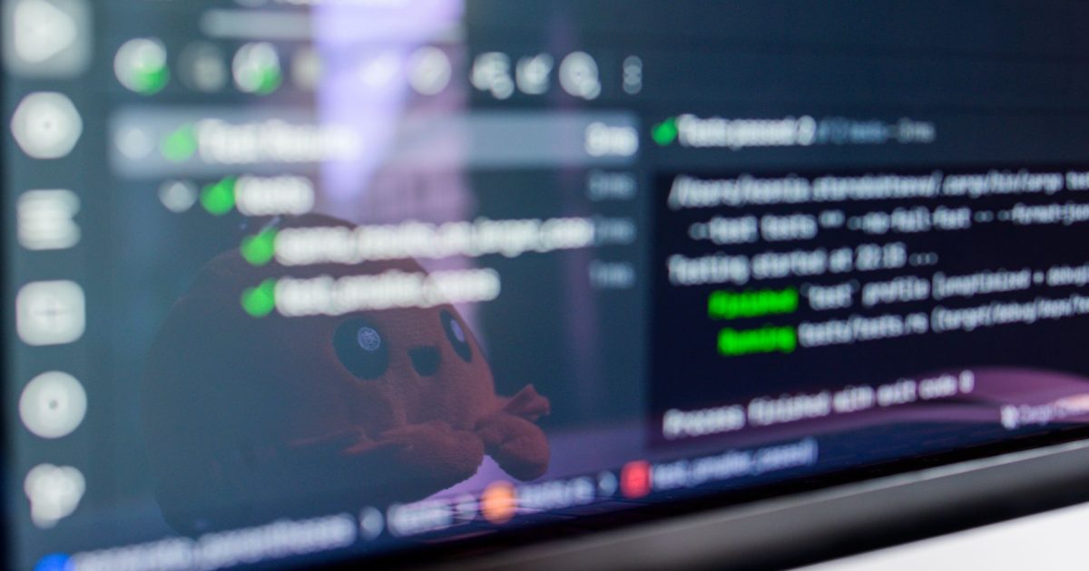Close-up of a laptop screen displaying programming code with a cute plush toy reflecting.