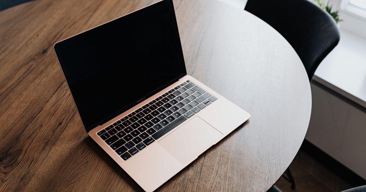 A sleek laptop rests on a round wooden table near a window, ready for work or study.