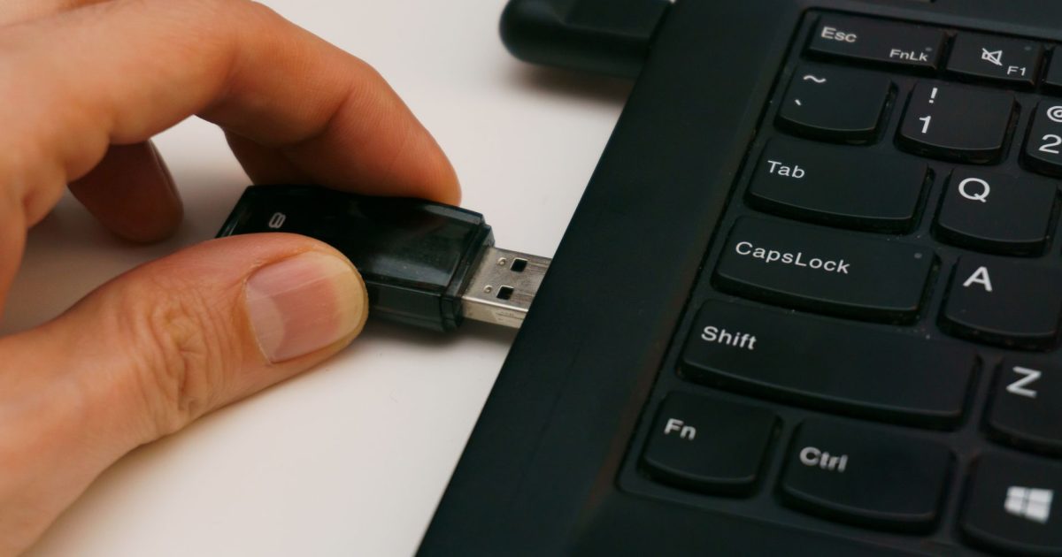 Close-up of a USB pen drive being inserted into a laptop USB port on a white surface.