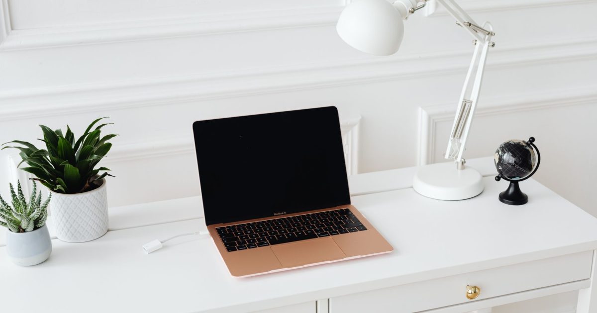 Clean and stylish workspace featuring a laptop, desk lamp, and potted plants on a white desk.