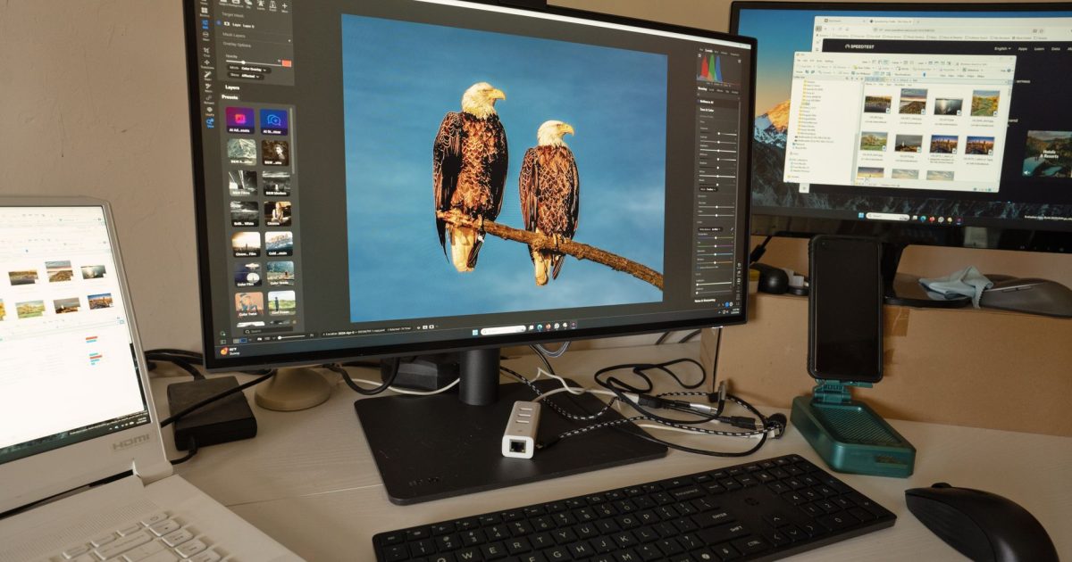 A desk setup showing photo editing software on multiple monitors, a keyboard, and peripherals.