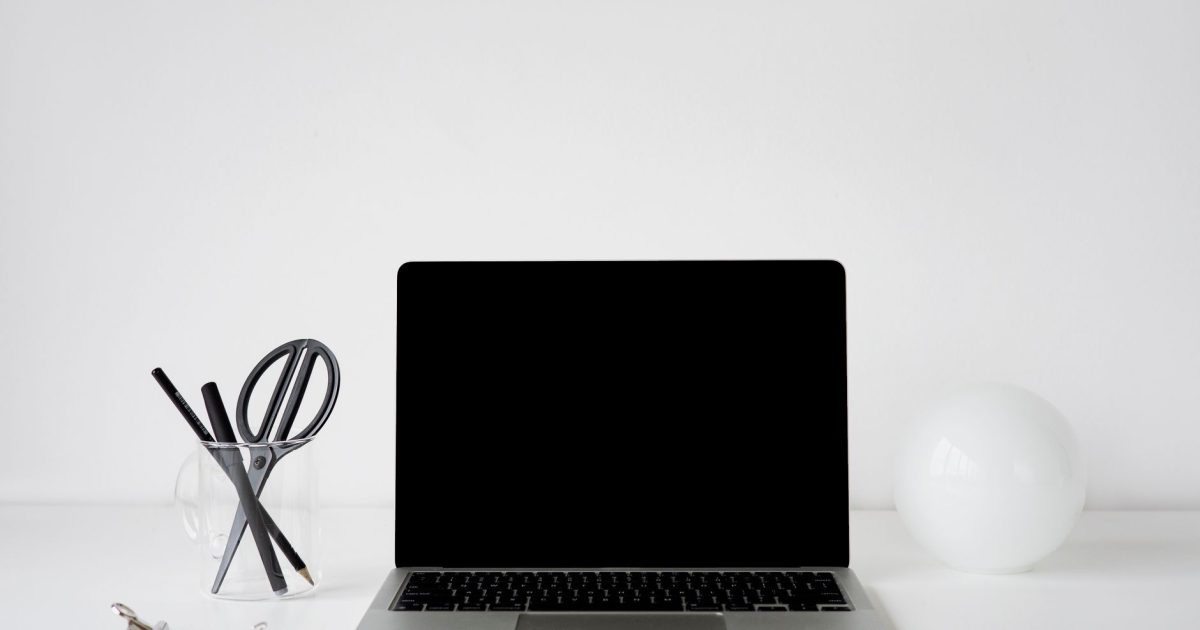 Modern minimalist office setup featuring a laptop, pens, and white decor elements on a white desk.