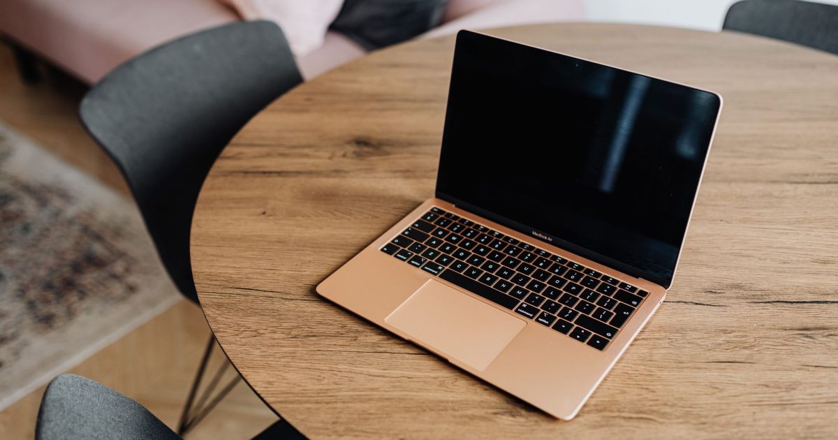 A modern laptop rests on a stylish round wooden table in a cozy room setting.