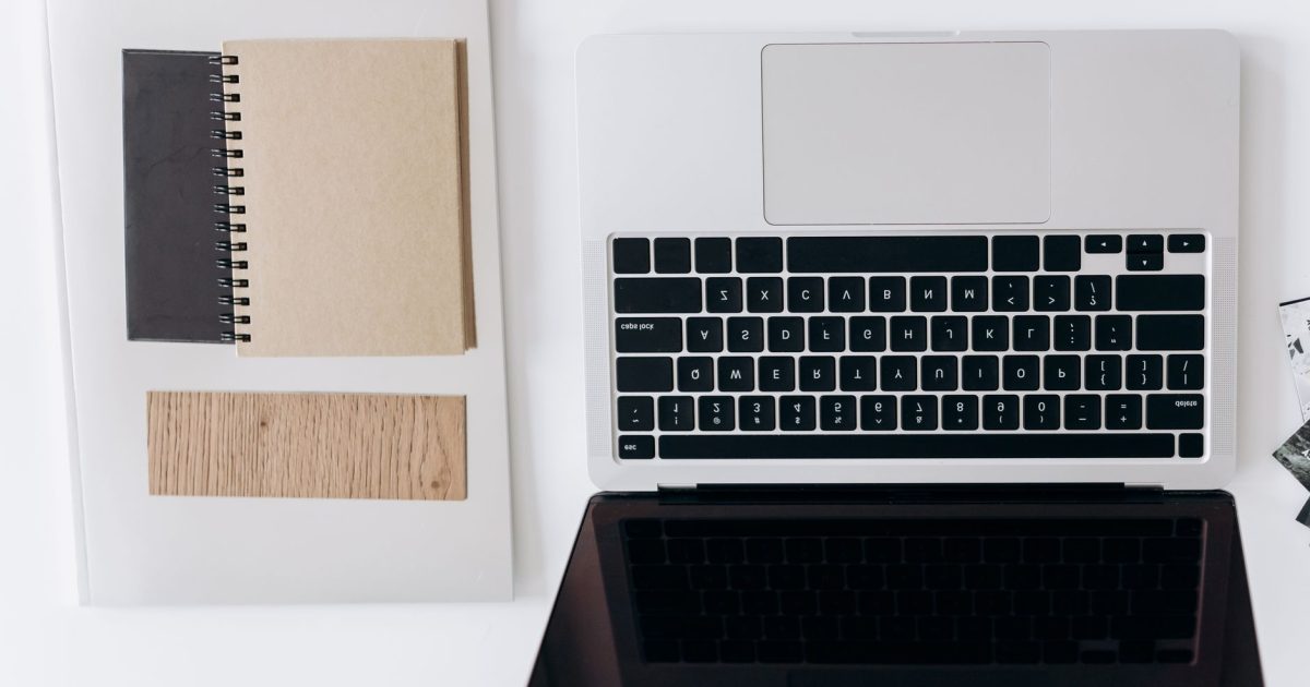 Top view of a minimalist workspace with a laptop and notebooks on a white desk.