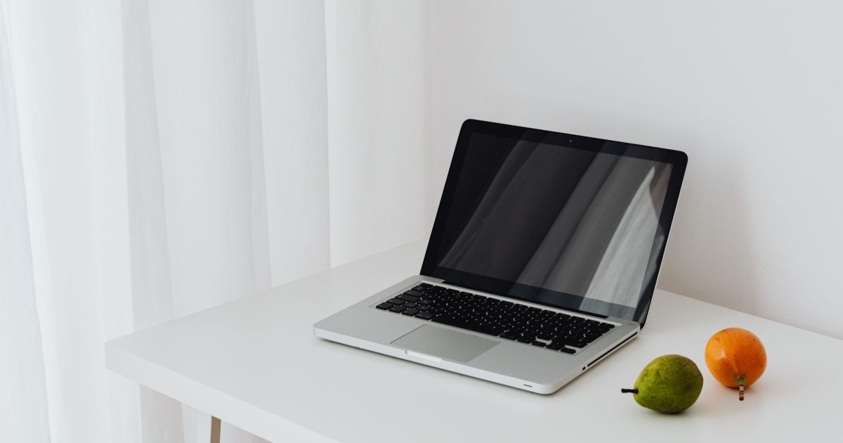 Modern minimalist workspace featuring a laptop and fresh fruit on a clean white table.
