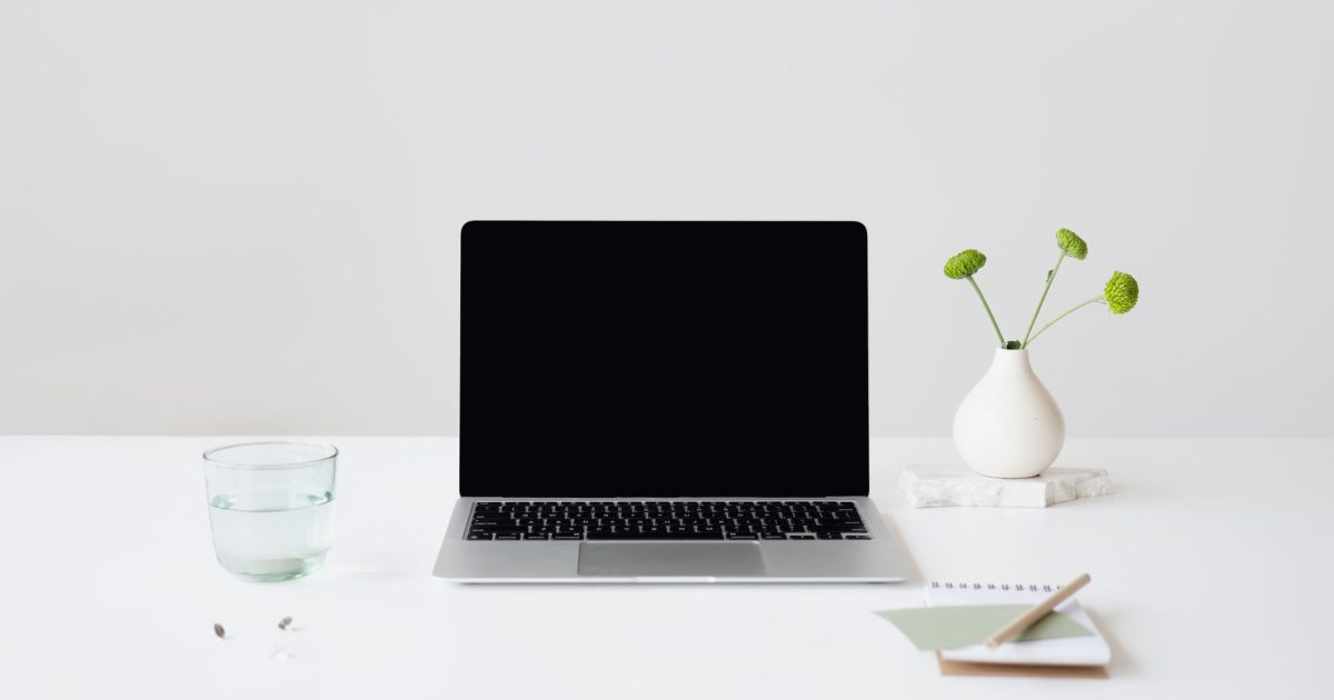 Simple minimalist workspace featuring a laptop, glass of water, and small plant on a white desk.