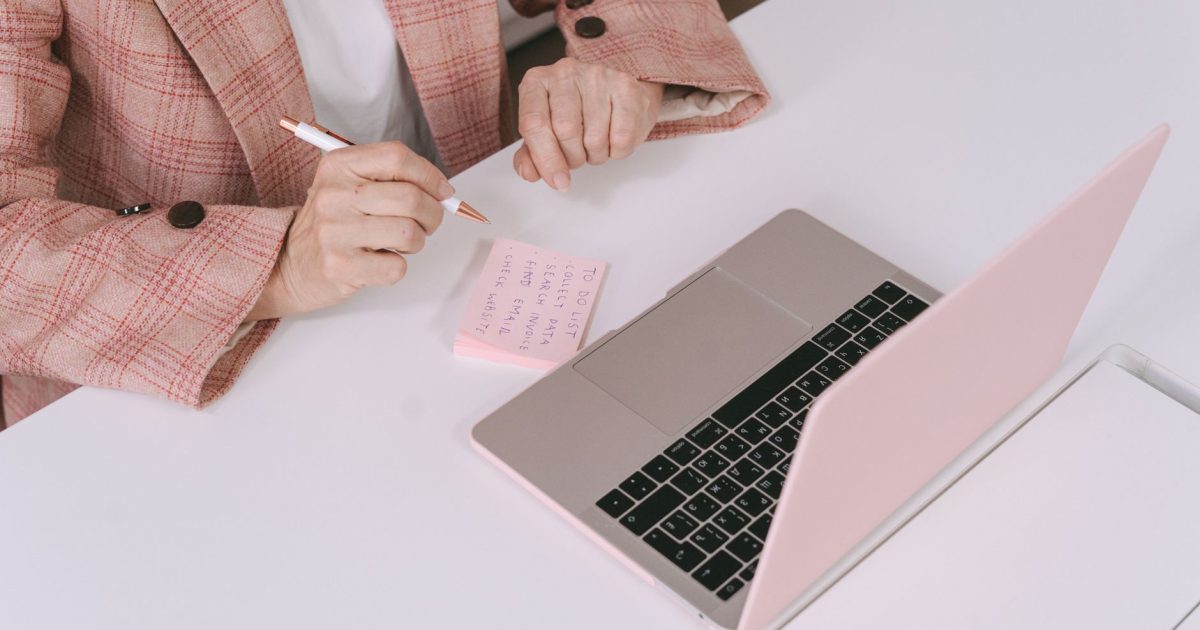 Businesswoman in a plaid jacket using a laptop and sticky notes for work planning.