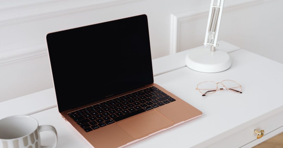 A modern sleek workspace featuring a laptop, desk lamp, and glasses on a white table.