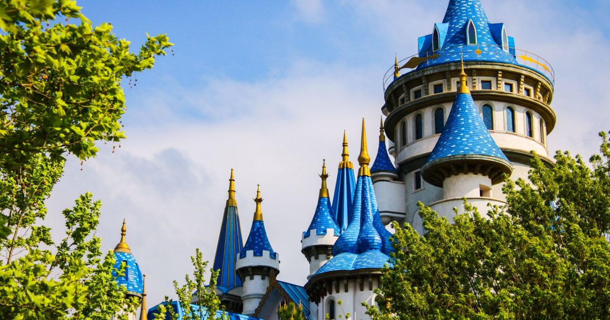 Stunning blue and white castle towers framed by vibrant greenery under a bright sky.