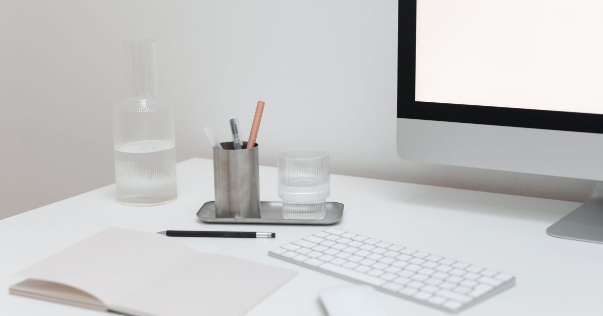 Modern computer with wireless keyboard and mouse on table with open notepad and bottle of water