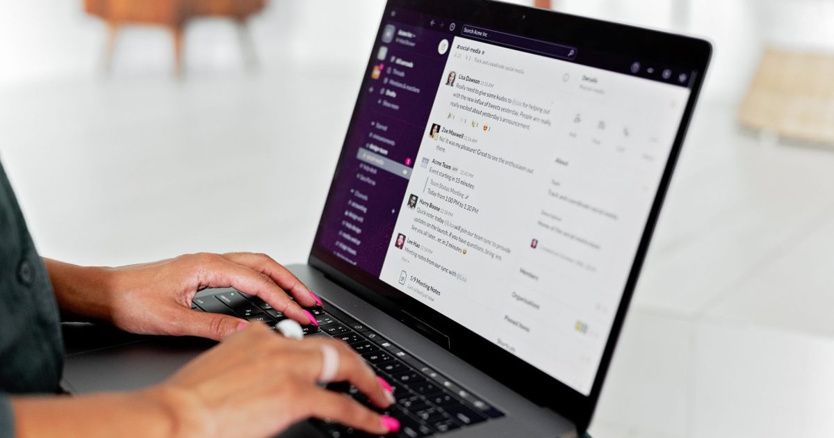 A woman types on a laptop using a messaging app in a modern office setting.