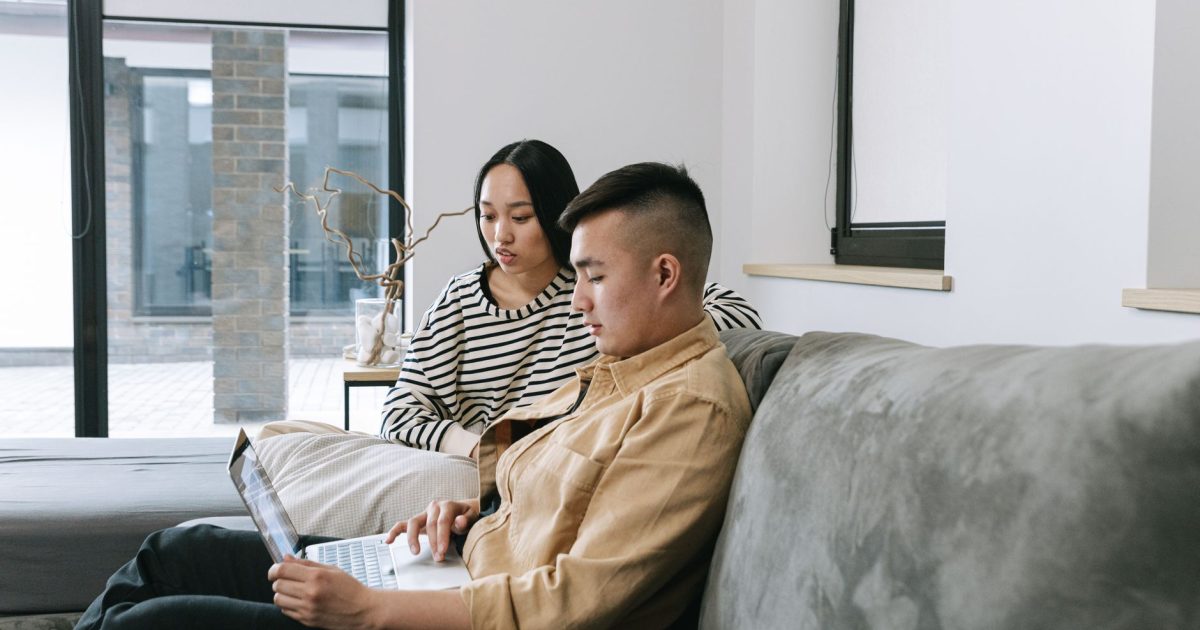 Two adults working from home in a cozy living room setting using a laptop.